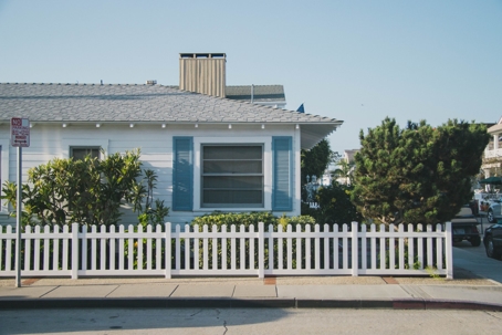 A white house with blue shutters, a white picket fence, and greenery.